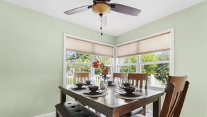 A dining area with a table set for four, a ceiling fan, and large windows with blinds. - Summer Home near Long Lake with Hot Tub & Firepit (Traverse City)