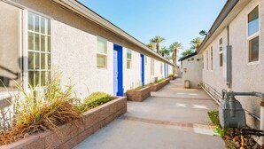 A row of single-story buildings with blue doors, a concrete pathway, and small planters. - Arts District Group Suite | Sleeps 10 + Pool Table (Las Vegas)