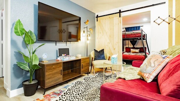 A modern living room with a large TV, a red sofa, a wooden cabinet, and a sliding barn door. - Arts District Group Suite | Sleeps 10 + Pool Table (Las Vegas)