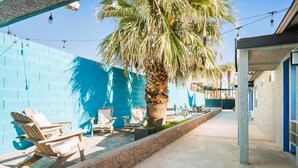 A poolside area with lounge chairs, a palm tree, and a blue wall. - Arts District Group Suite | Sleeps 10 + Pool Table (Las Vegas)