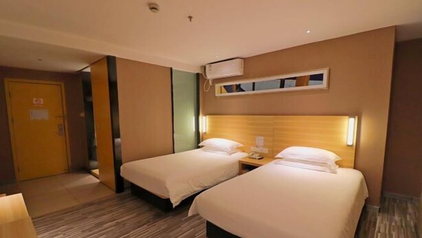 A hotel room with two beds, a wooden headboard, a bedside table with a lamp, and an air conditioning unit on the wall. - Tulou·He Hotel (Shanghai Songjiang New City Metro Station Branch) (Shanghai)