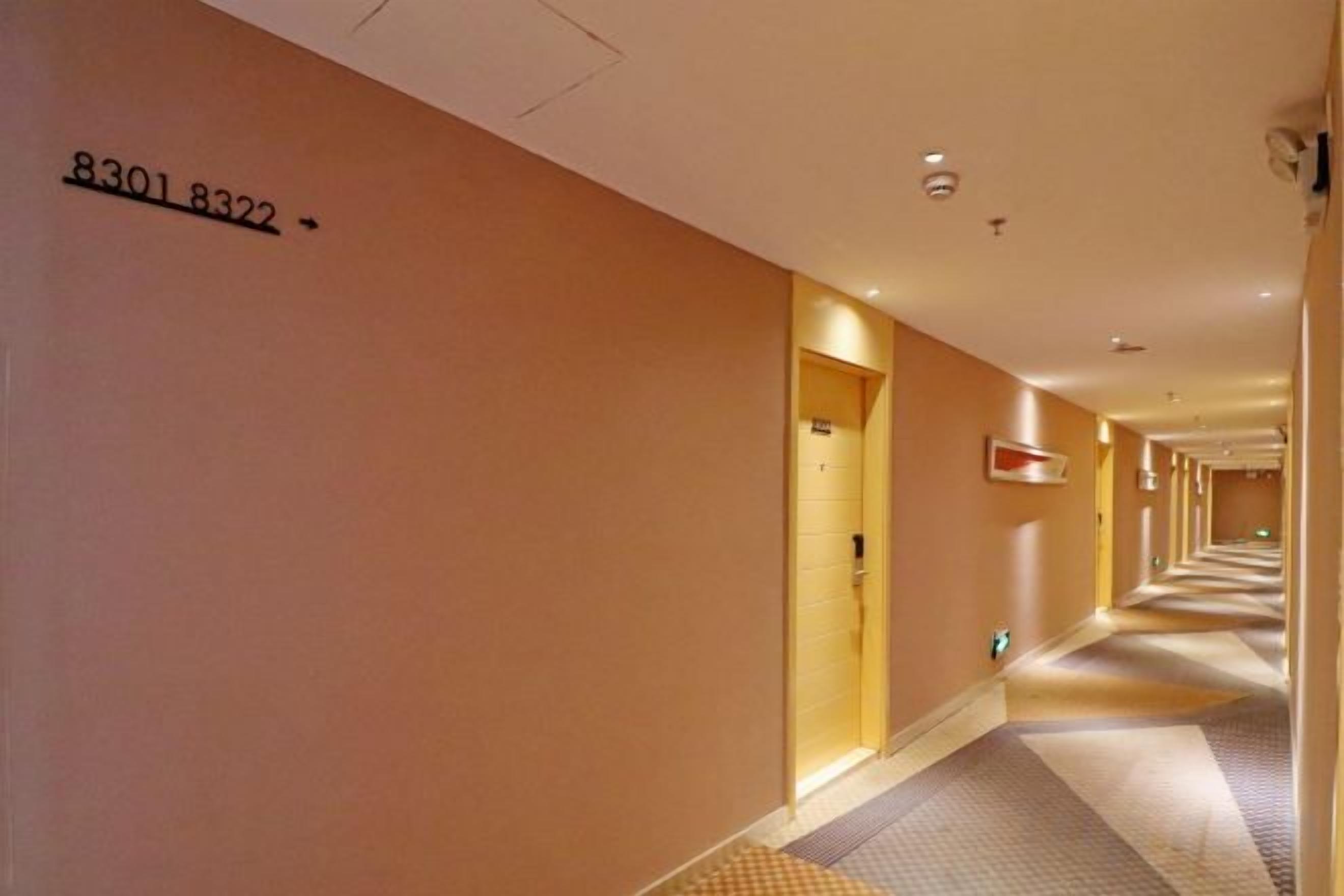 A hotel hallway with a number sign on the wall, doors on both sides, and a patterned carpet.