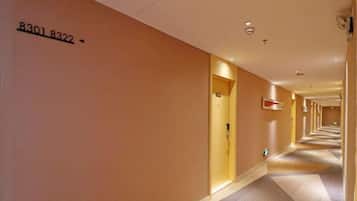 A hotel hallway with a number sign on the wall, doors on both sides, and a patterned carpet.