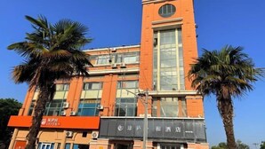 A multi-story building with a prominent clock tower, large windows, and palm trees in front. - Tulou·He Hotel (Shanghai Songjiang New City Metro Station Branch) (Shanghai)