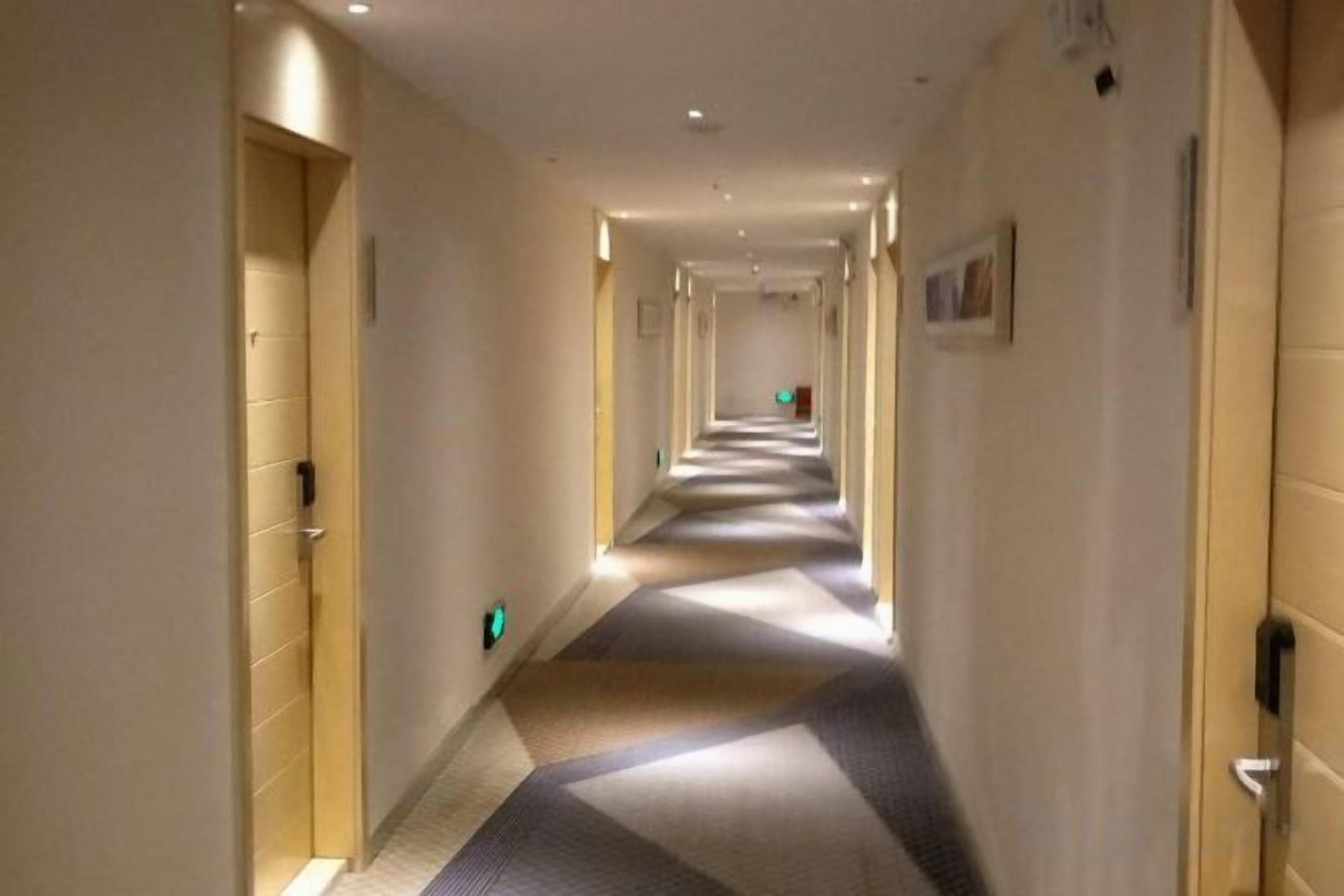 A hotel corridor with doors on both sides, a carpeted floor, and a light source at the end of the corridor.