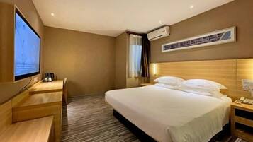 Una habitación de hotel con cama, escritorio, televisor y aire acondicionado.