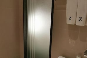 A bathroom with beige tiles, a glass shower enclosure, and two towels hanging on a rack with the letter 'Z' on them. - Tulou·He Hotel (Shanghai Songjiang New City Metro Station Branch) (Shanghai)