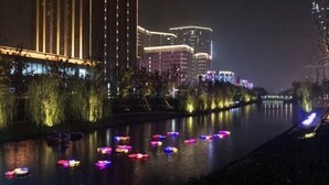 A river with illuminated boats, a well-lit building with vertical lines, and a cityscape in the background. - Tulou·He Hotel (Shanghai Songjiang New City Metro Station Branch) (Shanghai)