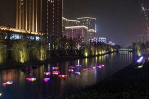 A river with illuminated boats, a well-lit building with vertical lines, and a cityscape in the background. - Tulou·He Hotel (Shanghai Songjiang New City Metro Station Branch) (Shanghai)