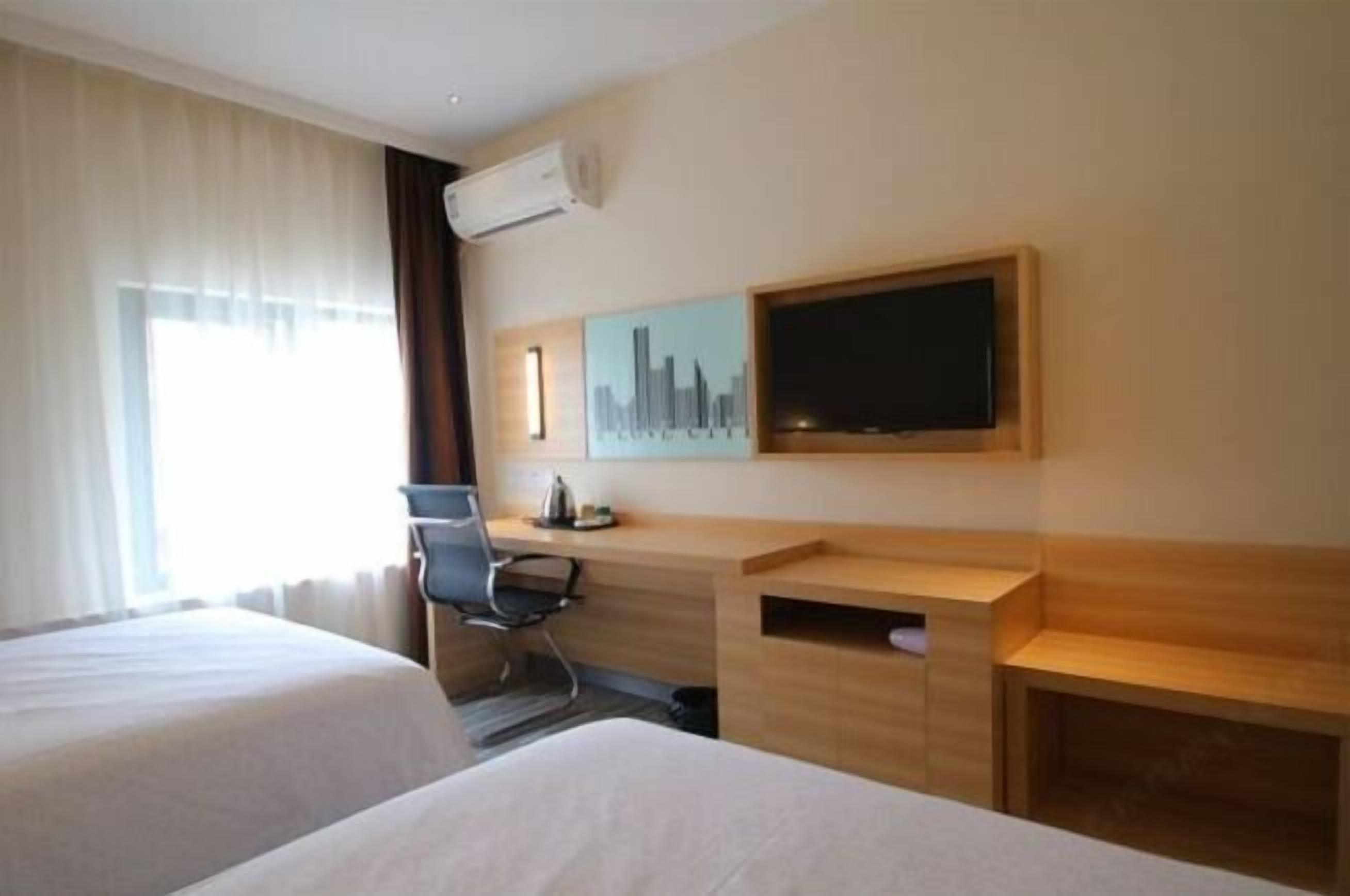 Hotellihuone, jossa on kaksi sänkyä, työpöytä, tuoli, taulutelevisio ja seinällä kaupunkimaisemaa esittävä taideteos.