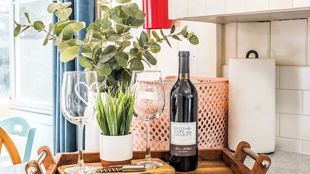 A wooden tray with wine glasses, a bottle, and a plant on a marble countertop.
