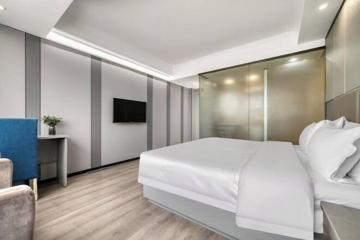 A modern hotel room with a large bed, a flat-screen TV, and a small desk with a plant.