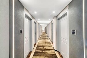 Pasillo de hotel con alfombra estampada, puertas a ambos lados y un cartel con los números de las habitaciones.