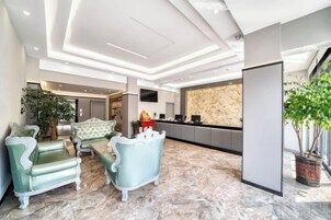 Un vestíbulo con mostrador de recepción, zona de estar con sillones y una planta grande en maceta.