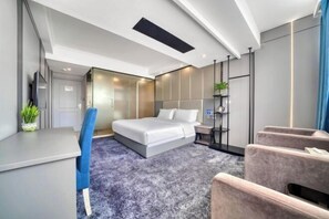 Ett modernt hotellrum med en säng, ett skrivbord, en stol och en liten sittgrupp.