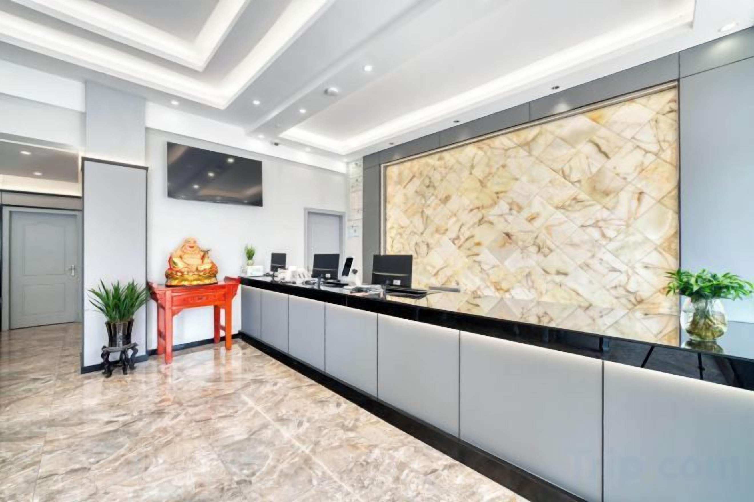 A reception area with a marble floor, a reception desk, a flat-screen TV, and a decorative statue.