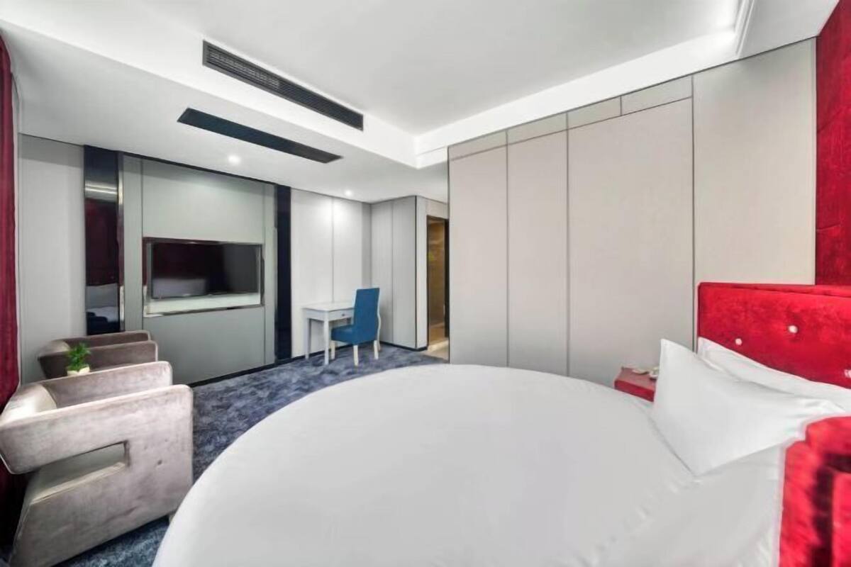 A modern hotel room with a large bed, a desk, a chair, and a television.