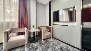 A modern hotel room with a grey carpet, two armchairs, a small round table with a plant, a TV mounted on the wall, and a window with sheer curtains. - Mingjue Business Hotel (Wenling)