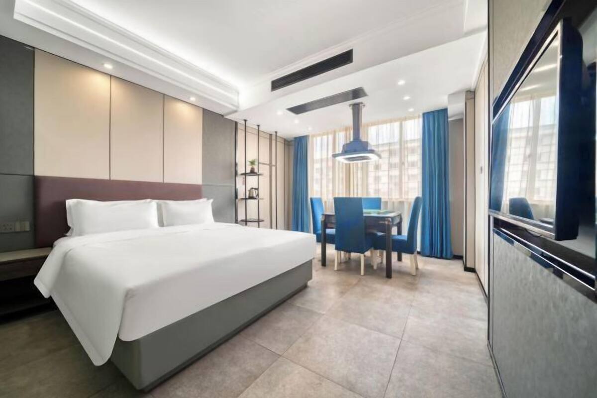 A modern hotel room with a large bed, a desk, and a dining area.