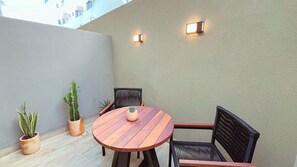 Un pequeño patio con una mesa redonda de madera y dos sillas, rodeado de plantas en macetas.