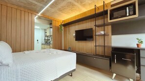 Una habitación de hotel moderna con una cama, una kitchenette y un televisor montado en la pared.