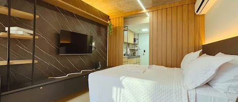 Una habitación de hotel moderna con una cama grande, un televisor de pantalla plana en la pared y un cabecero de madera.