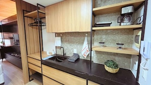 A compact kitchen with wooden cabinets, a black countertop, a coffee maker, and a small potted plant. - Setai Yacht Garden - By Almare Flats (João Pessoa)