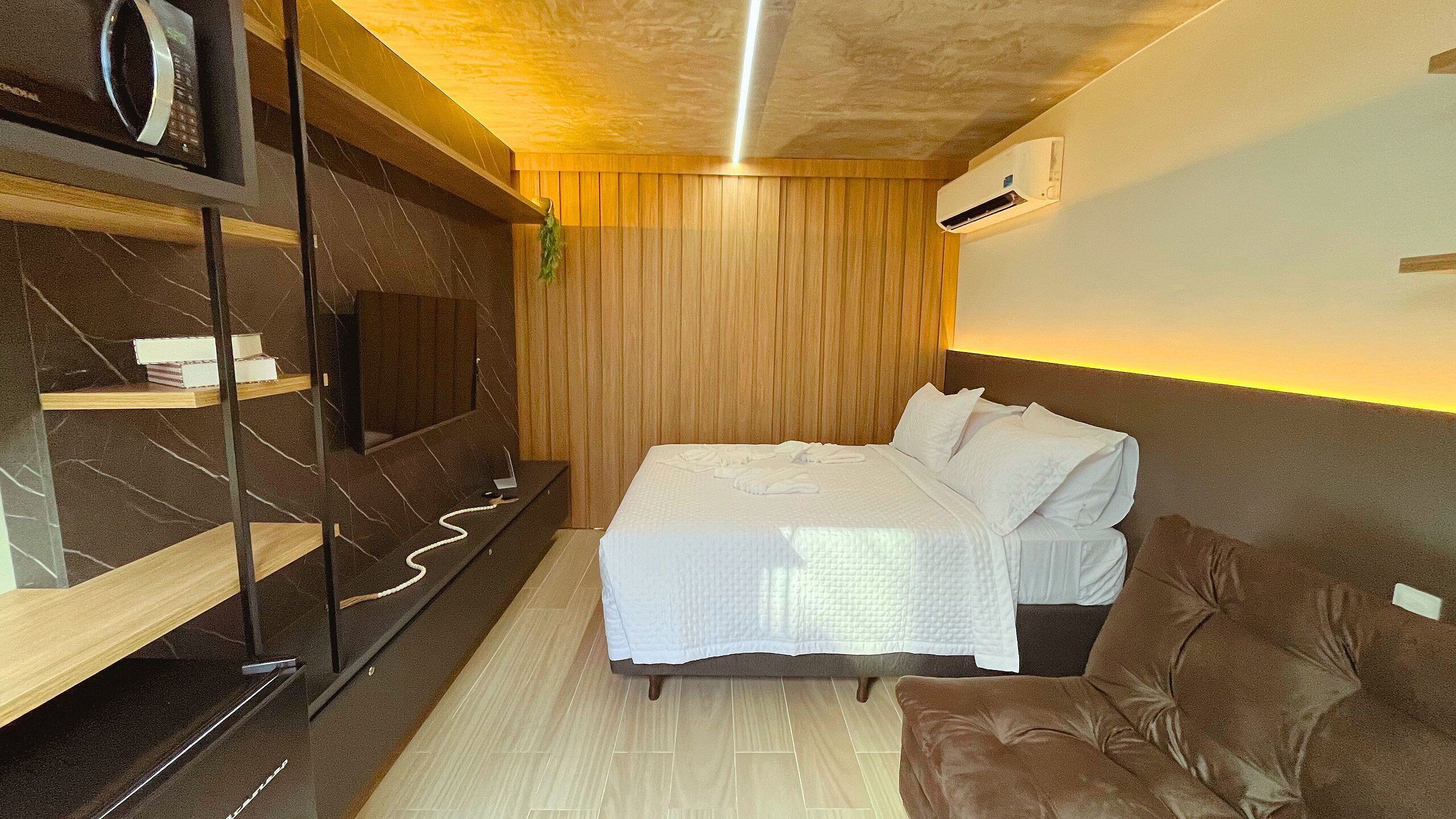 Ein Hotelzimmer mit einem Bett, einer Wandverkleidung aus Holz, einem eingebauten Fernseher und einer Wand-Klimaanlage.