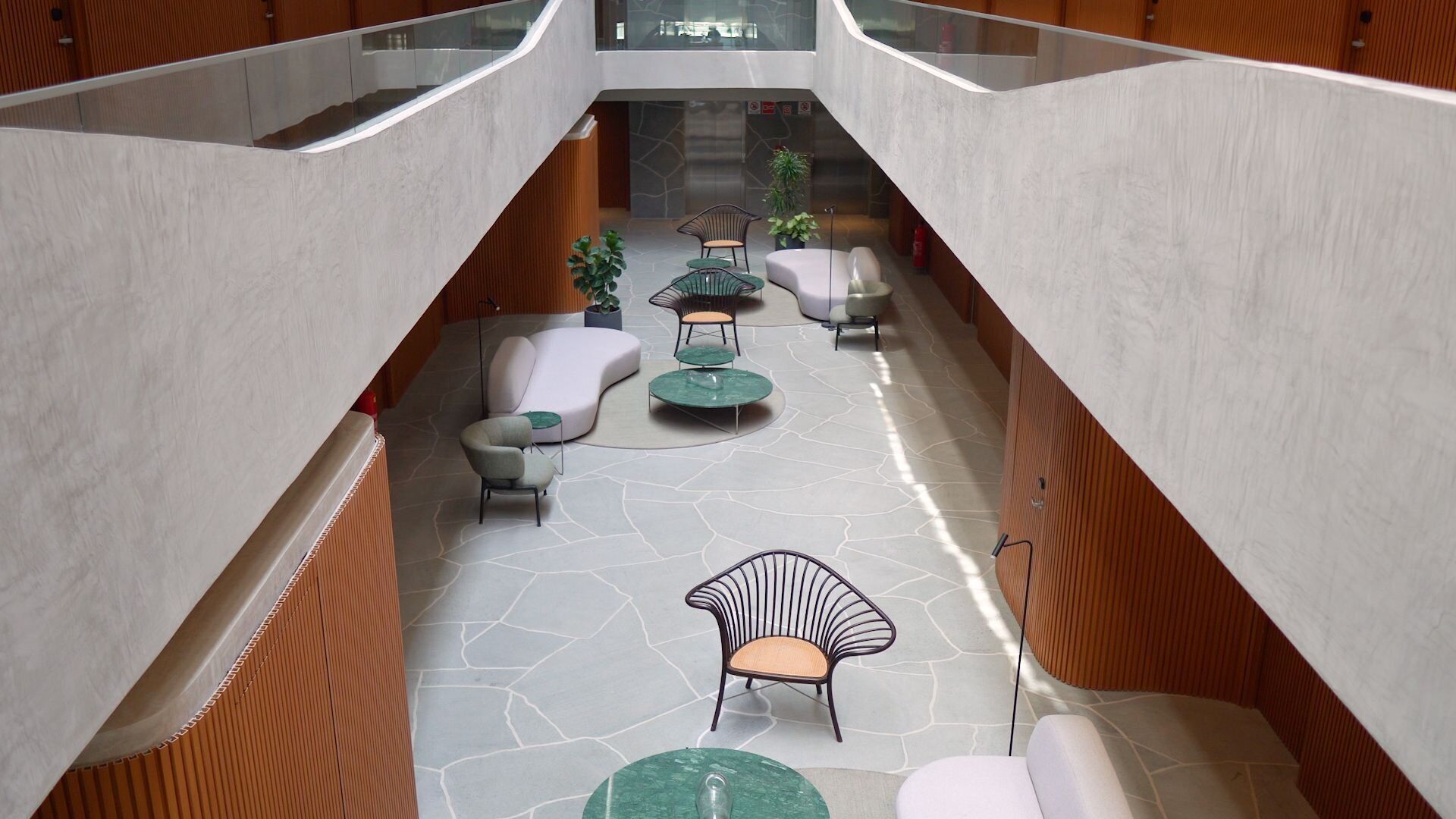 A spacious atrium with a central seating area, a staircase, and a glass railing.