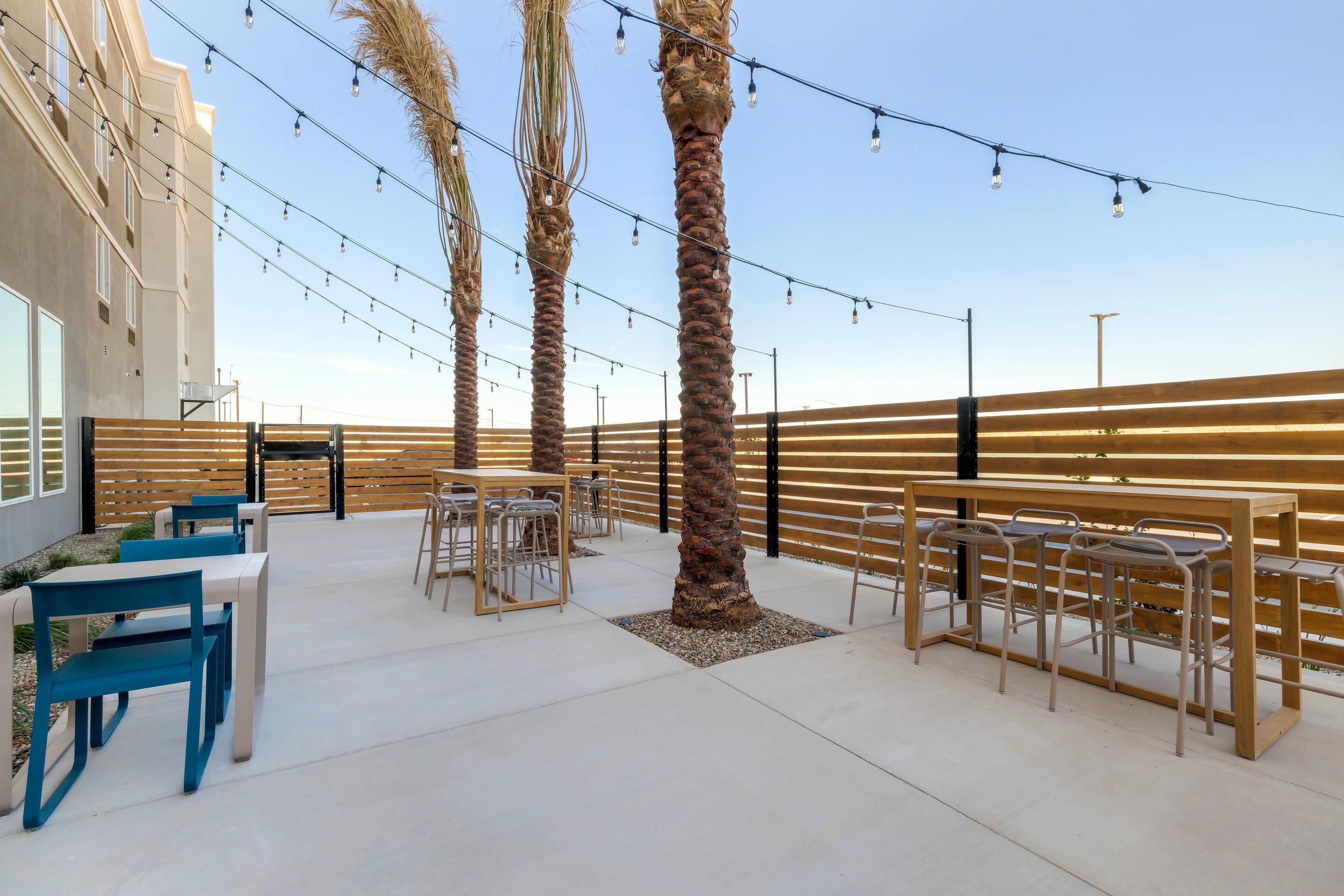 An outdoor seating area with tables and chairs, palm trees, and string lights.