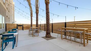 An outdoor seating area with tables and chairs, palm trees, and string lights.
