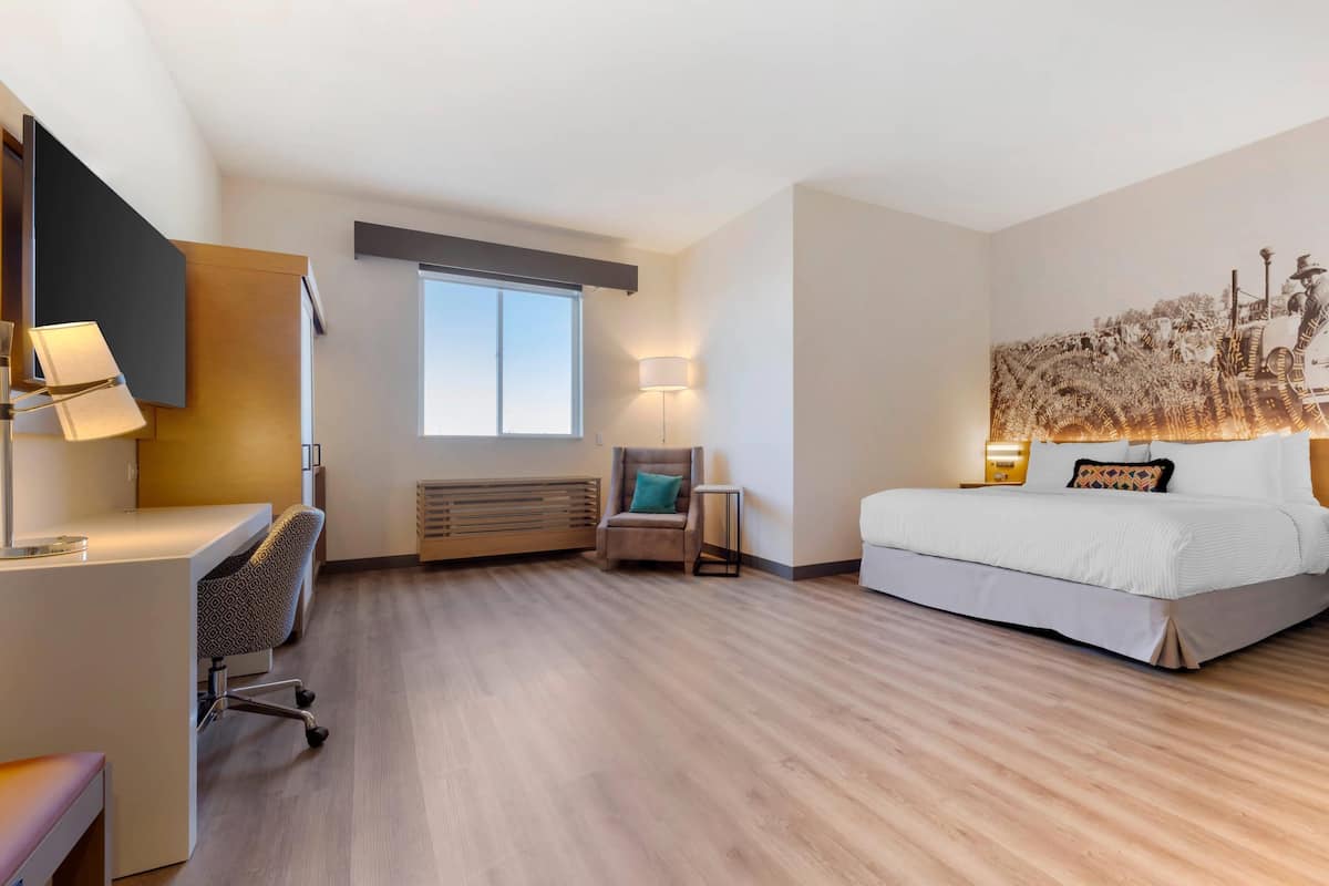 Una habitación de hotel con escritorio, silla, cama y una obra de arte en la pared.