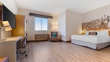 A hotel room with a desk, chair, bed, and artwork on the wall.
