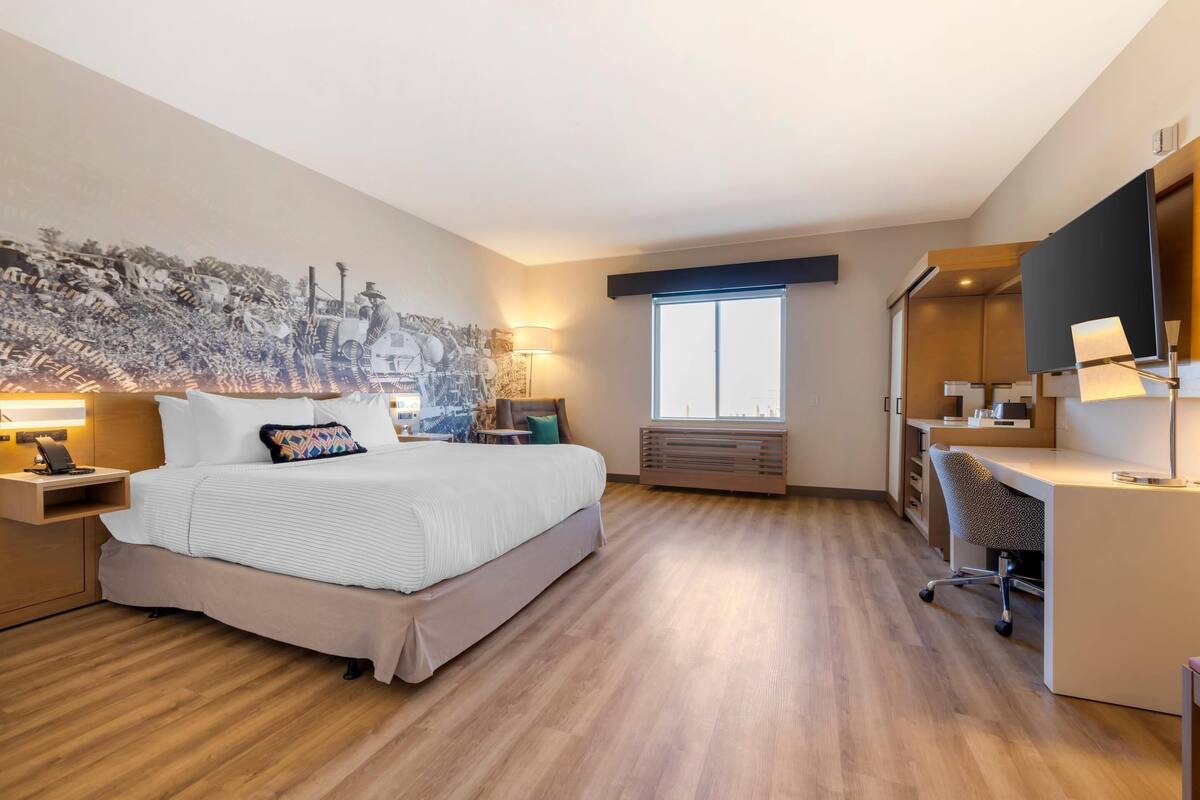 Habitación de hotel con una cama grande, un escritorio, una silla, una ventana y un televisor instalado en la pared.