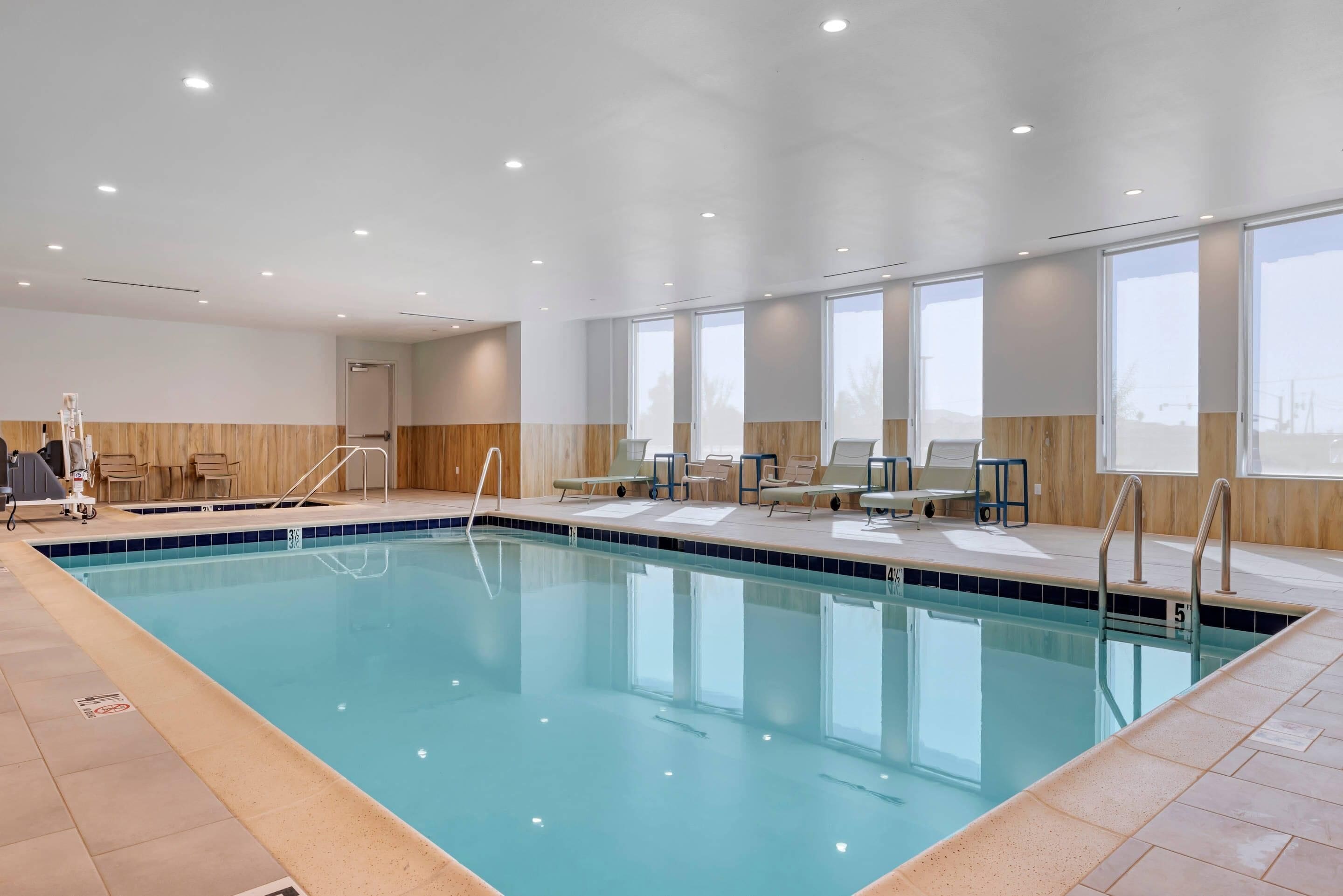 Una piscina interior con agua cristalina, rodeada de sillones de descanso y un muro de madera.