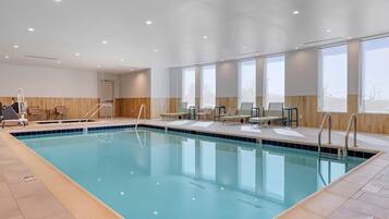 Una piscina interior con agua cristalina, rodeada de sillones de descanso y un muro de madera.