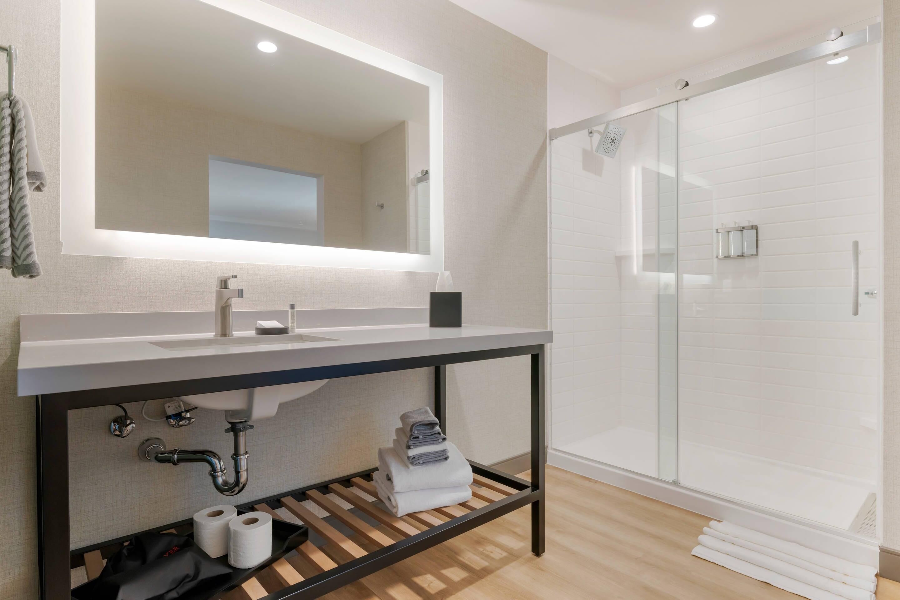 A modern bathroom with a large mirror, a sink, a shower, and a towel rack.