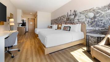 A modern hotel room with a large bed, a desk, and a chair. There is a mural on the wall and a small table next to the bed.