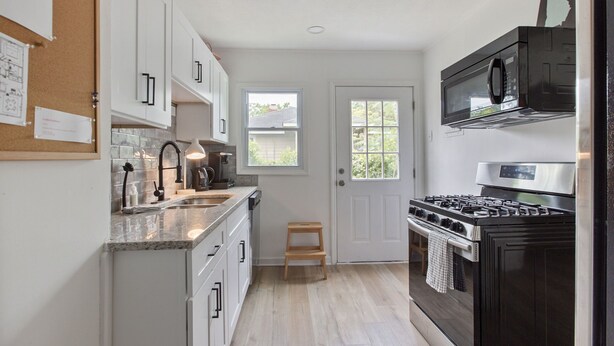 A compact kitchen with white cabinets, a black stove, a microwave, and a small wooden stool. - Modern Cottage in Columbus (Columbus)