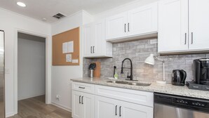 A modern kitchen with white cabinets, a granite countertop, a stainless steel dishwasher, and a coffee maker. - Modern Cottage in Columbus (Columbus)