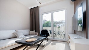 A modern living room with a sofa, a coffee table, a TV, and a balcony with a table and chairs. - Łódź Wólczańska - Workspace & Balcony - by Rentujemy (Łódź)