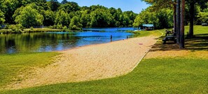 En park ved søen med sandstrand, græsplæner og en mindre bygning i baggrunden.