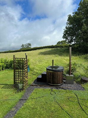 A hot tub in a grassy outdoor area with a wooden fence and a tall chimney.
