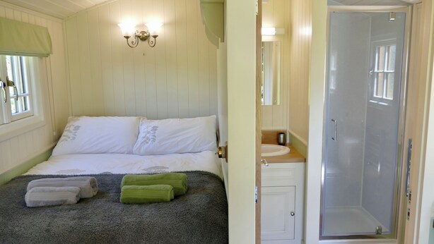 Een slaapkamer met een bed, een badkamer met een wastafel en spiegel, en een douche.