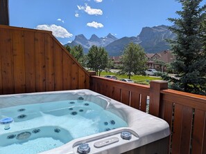 A hot tub with a wooden deck, surrounded by mountains and trees. - Designer Home, Private Hot Tub (Canmore)