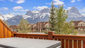 A balcony with a view of snow-capped mountains and a row of traditional chalet-style buildings. - Designer Home, Private Hot Tub (Canmore)