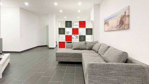 Una sala de estar moderna con un sofá seccional gris, una mesa de centro blanca y un mueble decorativo para pared rojo y negro.