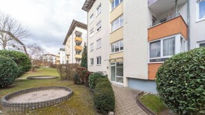 Un edificio residencial de varios pisos con balcones, un patio empedrado y arbustos bien cuidados.
