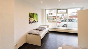 Una habitación pequeña y moderna con una cama individual, un ventanal grande y vistas a la calle.