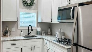 Une cuisine moderne avec des meubles blancs, un réfrigérateur en acier inoxydable, un four à micro-ondes et une cuisinière à gaz.